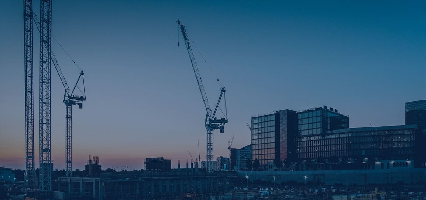 Cranes operating at urban construction site during sunset